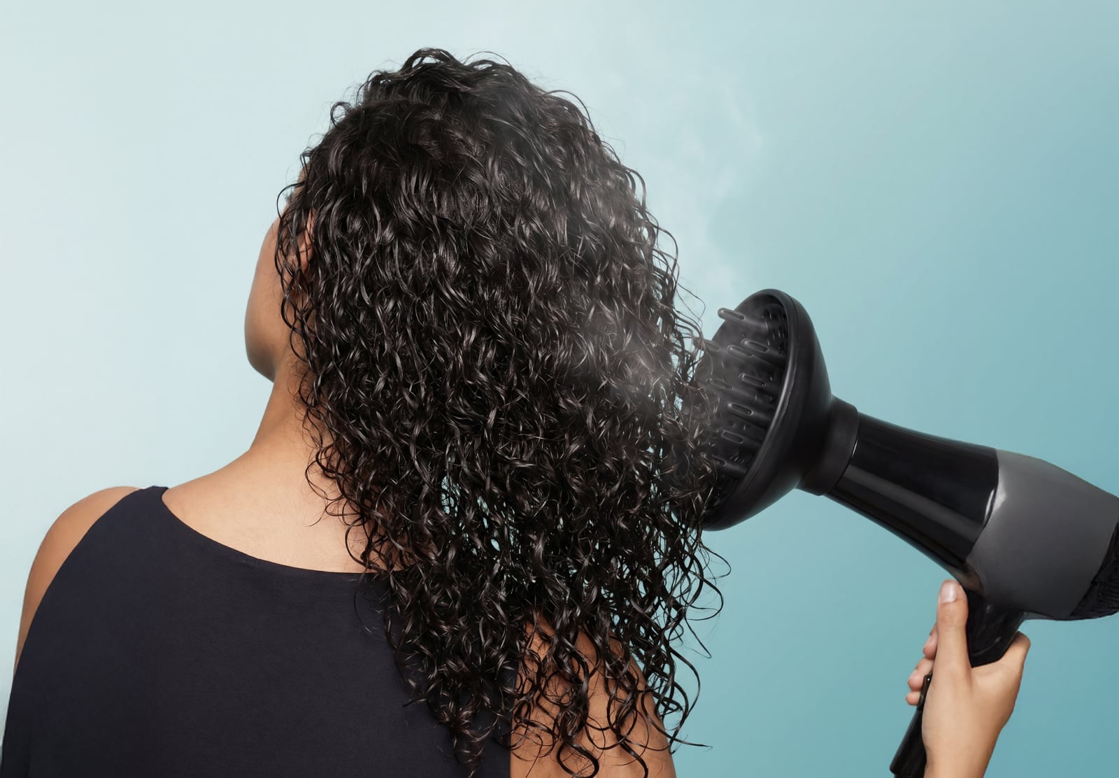 Image of a woman difussing her curly hair on a teal gradient background